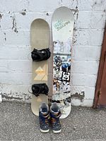 Two snowboards and one pair of snowboard boots arranged upright against a wall