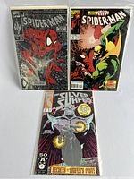 Three comics in protective sleeves arranged on white surface, showing the full front cover of two Spider-Man comics and one Silver Surfer comic.