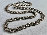Photo showing the full length of the triple strand sterling silver necklace laid out on a flat surface to highlight the braided box link pattern and metal shine.