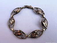 Front view of vintage gold bracelet with seven scrolled leaf design links arranged in a circular layout on a white fabric background.