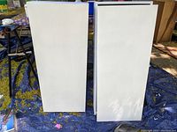 Closed view of two white primed medicine cabinets standing upright outdoors on a tarp.