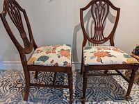 Pair of matching solid wood chairs with dark finish, carved backs, and floral patterned seats.