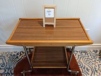 Front and top view of the vintage teak and laminate bar cart showing the top tier with teak trim and laminate surface.