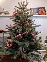 Full view of the artificial Christmas tree showing green synthetic needles, branches, and the red twisted garland wrapped around it, standing on the floor indoors.