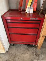Front view of closed red metal Craftsman toolbox on wheels showing brand logo and visible wear.