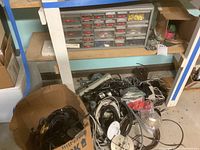 Organizer with multiple labeled small drawers containing assorted fuses and electrical connectors. Various loose cables and electrical components piled below on floor.