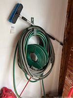 Two round hoses and two flat hoses coiled and hanging on a wall hook with a cleaning brush attached to the hook.