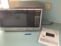 Front view of Panasonic microwave showing stainless steel door and keypad, along with user manual placed beside it.