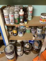 Full shelf view of various spray paint cans, wood hardener, and paint thinner along with small finishing product bottles.