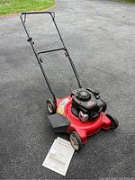 Full view of the MTD push lawn mower with manual placed on the ground in front of it, showing the handlebar, deck, and engine.