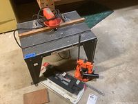 Full view of Sears Craftsman router table with attached Sears router and assorted clamps and accessories around it on basement floor.