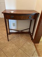 Full front view of the wooden side table showing the curved drawer front and metal handles.