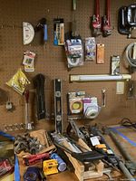 Wide shot showing pegboard and workbench with various hand tools, pipes, hardware and packaging. Lighting fixture visible but excluded from lot.