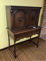 Full view of the dark wood one-piece antique server hutch with upper cabinet and lower drawer, standing on carved turned legs and stretchers.