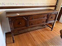 Front view of the antique wooden sideboard showing two cabinet doors and two central drawers with metal drop pulls and wood knobs, standing on turned legs with finial detailing.