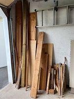 Photo of multiple wood boards, plywood, and treated post leaning against a wall in a garage.