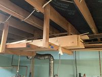 Wide view of pine lumber boards stored horizontally under basement rafters.