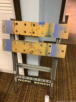 Work bench frame showing yellow and blue wood panels with circular holes, metal legs, and 'WORK BENCH' label at bottom.