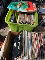 Two boxes containing approximately 100 vintage 12-inch 45 RPM vinyl records with worn album covers visible.