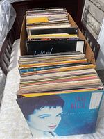 Top-down view of long cardboard box filled with over 100 12-inch vinyl records showing colorful album covers slightly worn with some moisture damage.