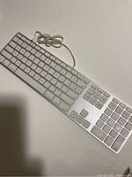 Full view of Apple wired keyboard with cable visible, showing overall keyboard layout and design.