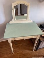 Full view of child's vanity table showing off-white wooden frame, green top, single drawer with knob, and attached mirror.