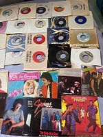 Photo showing a spread of 45rpm vinyl singles with various illustrated sleeves including Kim Wilde, Don Henley, Survivor, Scandal, and others.
