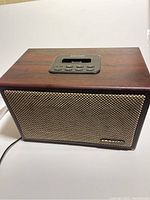 Front view of wooden Crosley speaker dock with control buttons on top and woven beige front grille.