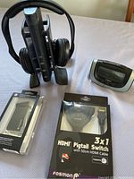 Photo showing Sennheiser wireless headphones on charging stand, Fosmon HDMI switch box, Motorola device, and power adapter on table.