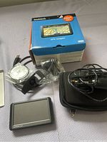 Full lot with Garmin Nuvi 255w GPS unit, box, mounting accessories, cables, installation CD, and carrying case on fabric surface.