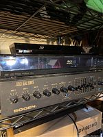 Photo showing Bogen Gold Seal Series amplifier with multiple mic controls and Sony Blu-ray players stacked on a shelf.