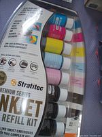 Photo of Stratitec Premium Series inkjet refill kit with multiple bottles of ink in different colors visible through plastic packaging.