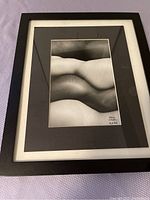 Framed black and white artistic nude photograph laid on purple surface.