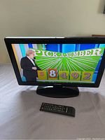 Front view of the Polaroid 24-inch LED TV showing a colorful game show screen with remote control in front.
