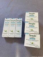 Three Simple Hydrating Booster bottles and three Simple Skin Quench Sleeping Cream boxes on a fabric surface.