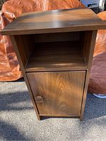 Front view of the small wooden end table showing the woodgrain finish, open shelf, and closed cabinet with knob door.