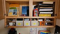 Shelf with mailing envelopes, cards, paper stacks, colorful pencils on top, multiple labeled organizer bins below