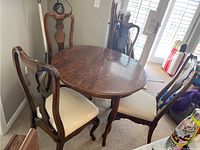 Dining table and four chairs arranged in a corner, showing table with leaf and chairs with light-colored fabric seats