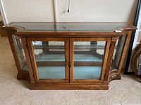 Front view of wooden framed glass display cabinet with glass doors and curved glass sides. Shows damage to handle and bottom trim.