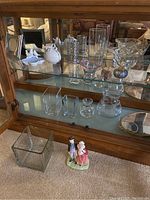 Various clear glass vases, square bowls, and a glass pitcher inside a wooden glass display cabinet.