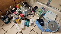Photo of all hair care and cleaning products spread on bathroom floor and counter, showing variety of bottles, sprays, boxes, and hair styling tools.