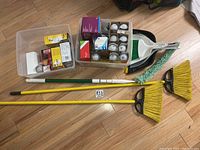 Full lot overview showing boxes of light bulbs, brooms including a yellow broom, smaller broom, two dust pans and a green/white extendable duster.