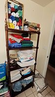 Wood shelf unit holding assorted linens, towels, pillows, fabric pieces