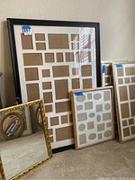 Three mirrors and wall frames leaning against wall, showing various frame styles and sizes.