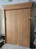 Front view of closed wood veneer cabinet with two-panel doors and crown molding top