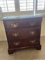 Front view of the wood nightstand showing four drawers with brass handles and glass top.
