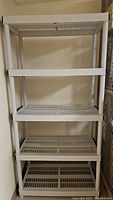 Front view of assembled plastic shelving unit showing five lattice shelves and cylindrical supporting posts.