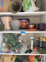 Multiple shelves of plant pots, faux greenery, gardening tools, and potting soil supplies captured to show lot contents