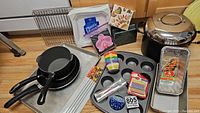 Overview of cookware and baking items including frying pans, stock pots, jelly roll pan, muffin tin, loaf pans, cooling racks, plates, napkins, granite holder, metal skewers, baking cups, birthday candles