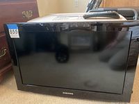 Front view of the Samsung flat-screen television showing the black bezel and screen, with a remote control placed on top of the TV.